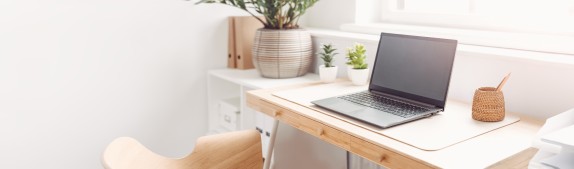 Helles, modern eingerichtetes Homeoffice mit Holzschreibtisch, aufgeklapptem Laptop, kleinen Zimmerpflanzen und minimalistischer Dekoration in natürlichem Licht.