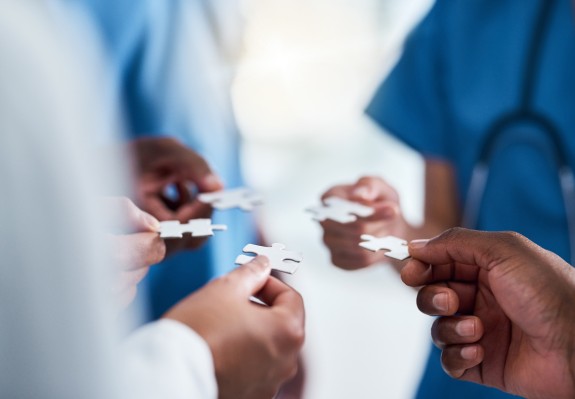 Mehrere medizinische Fachkräfte in blauer und weißer Kleidung halten jeweils ein Puzzlestück in der Hand – symbolische Darstellung für Teamarbeit und Zusammenarbeit im Gesundheitswesen.